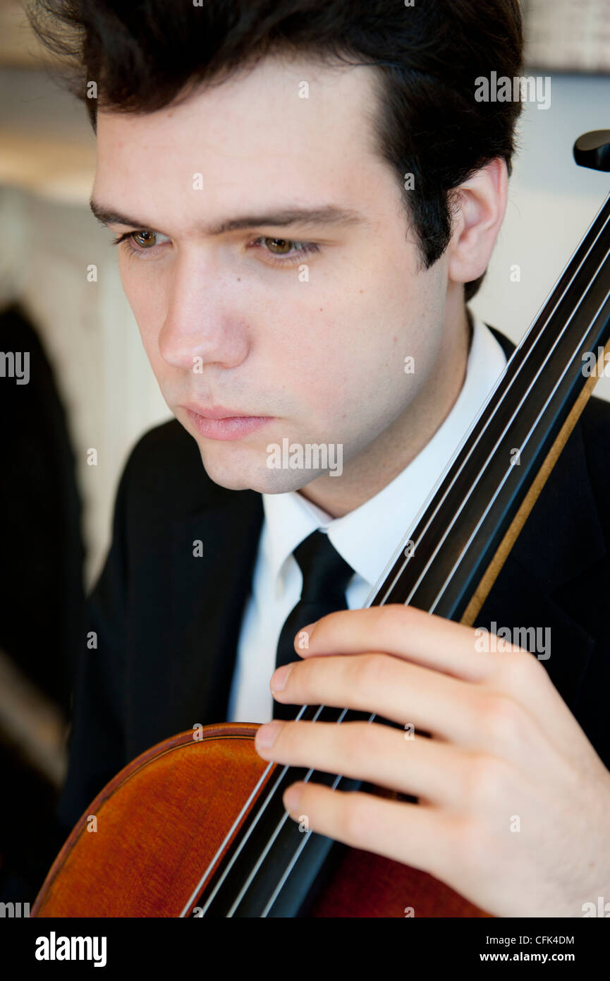 Bel giovane uomo che indossa una tuta e tiranti a suonare il violoncello Foto Stock