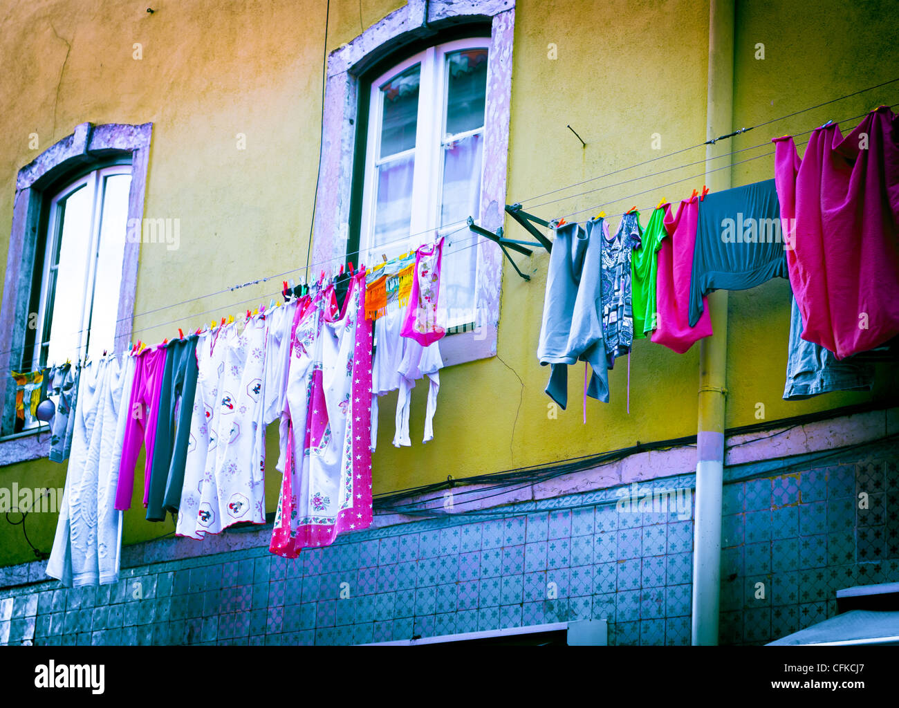 Le vecchie finestre con colorati servizio lavanderia incernierata su una linea di lavanderia a Lisbona Portogal, portoghese servizio lavanderia su giallo e blu di parete. Foto Stock