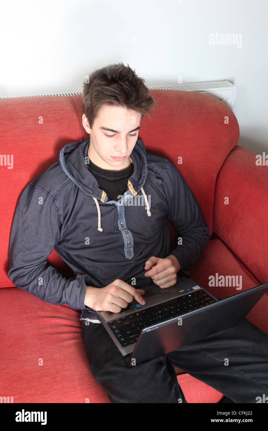 Giovane maschio seduto da solo utilizzando un computer portatile. Foto Stock
