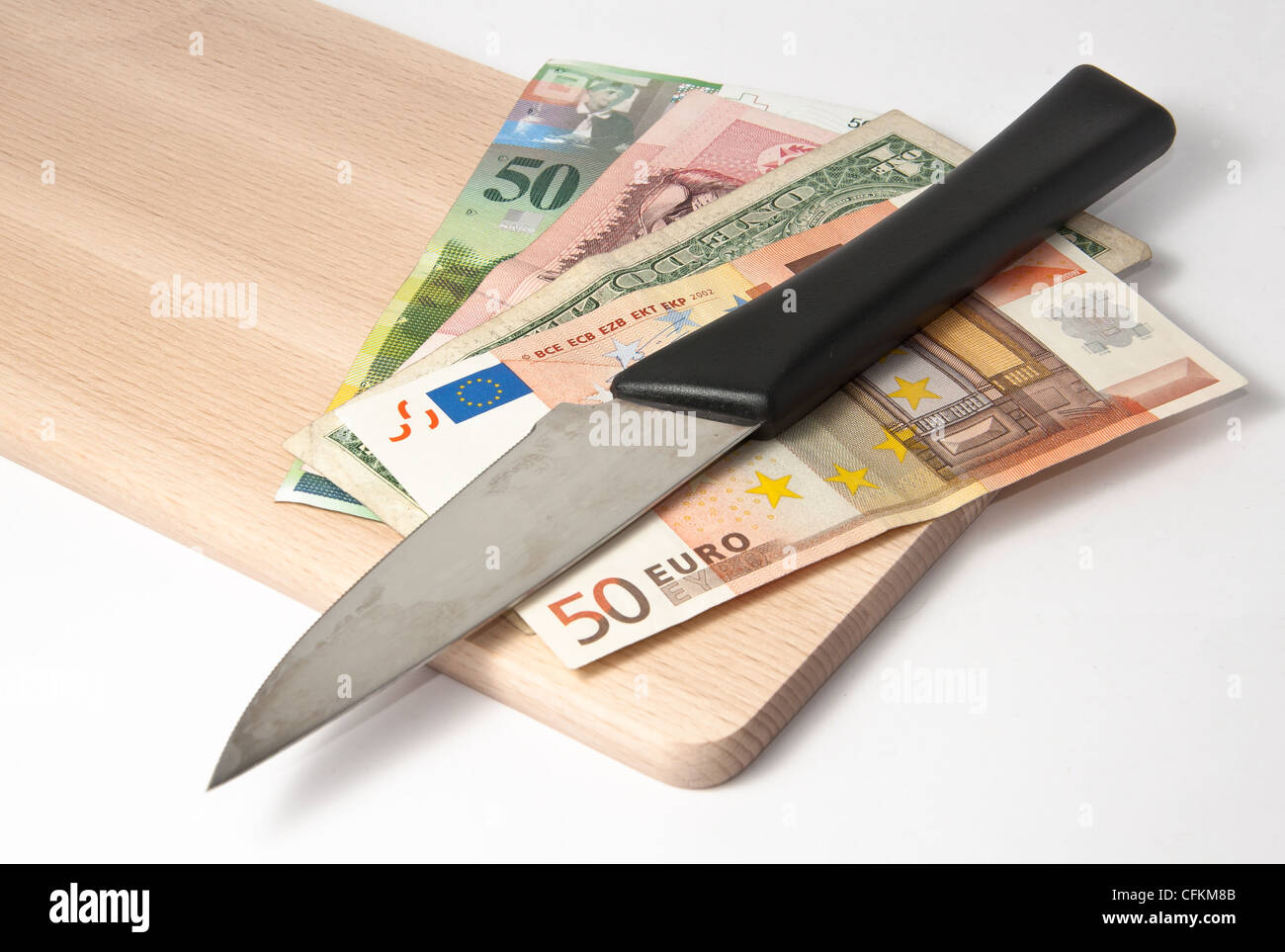 Diverse banconote in valuta sotto un coltello su un tagliere Foto Stock