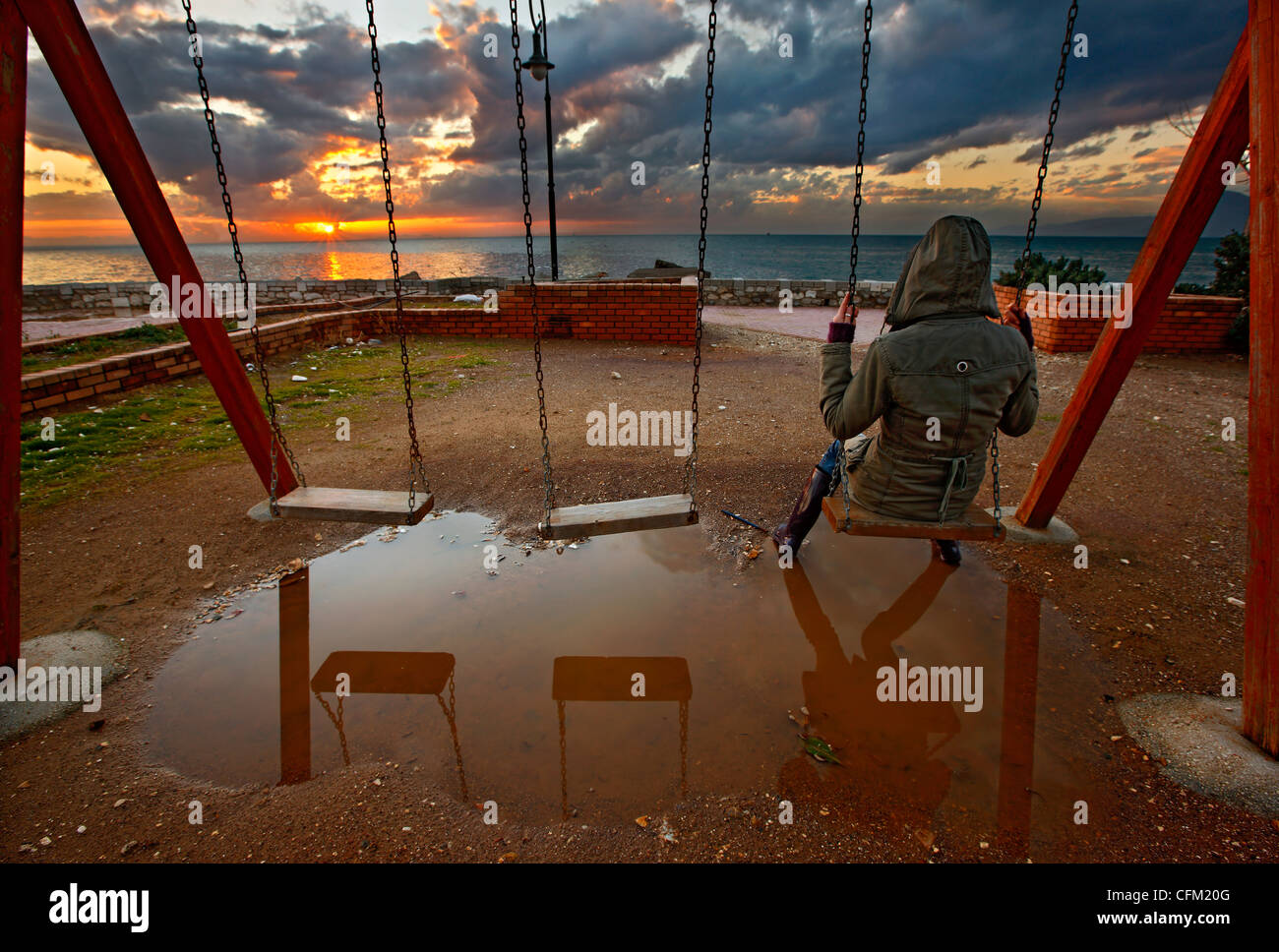 Una ragazza solitaria su altalena, proprio accanto al faro di Patrasso, godendo del tramonto. Achaia, Peloponneso, Grecia Foto Stock