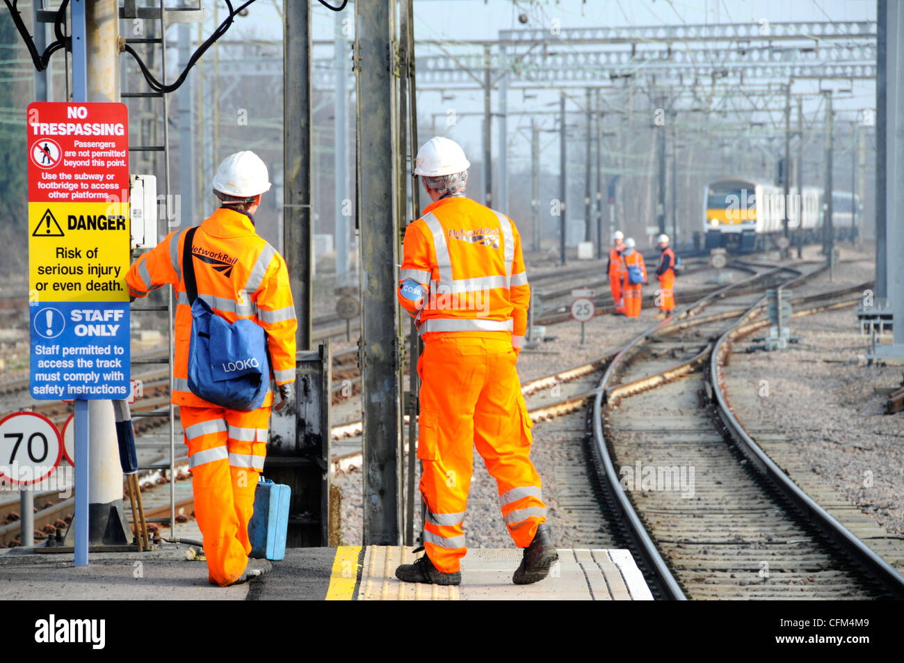 Cartello e vista posteriore giacca alta visibilità Network Rail Workmen e elmetto su piattaforma ferroviaria gruppo di lavoratori su Tracce oltre treno distante Essex Inghilterra UK Foto Stock
