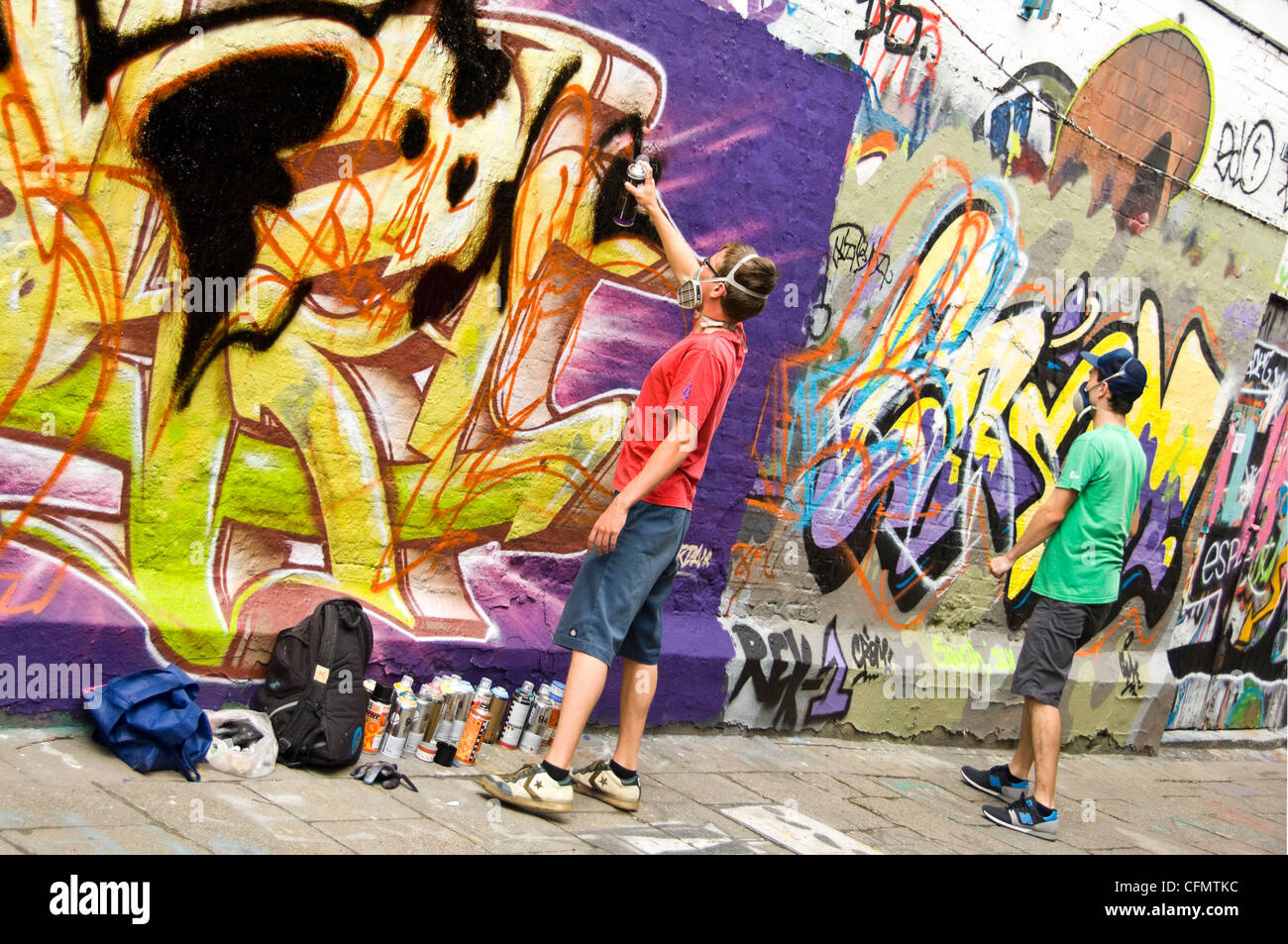 Vista orizzontale di Graffiti Vicolo Werregaran Straat a Gand, con due artisti verniciatura a spruzzo la loro arte sul marciapiede parete. Foto Stock