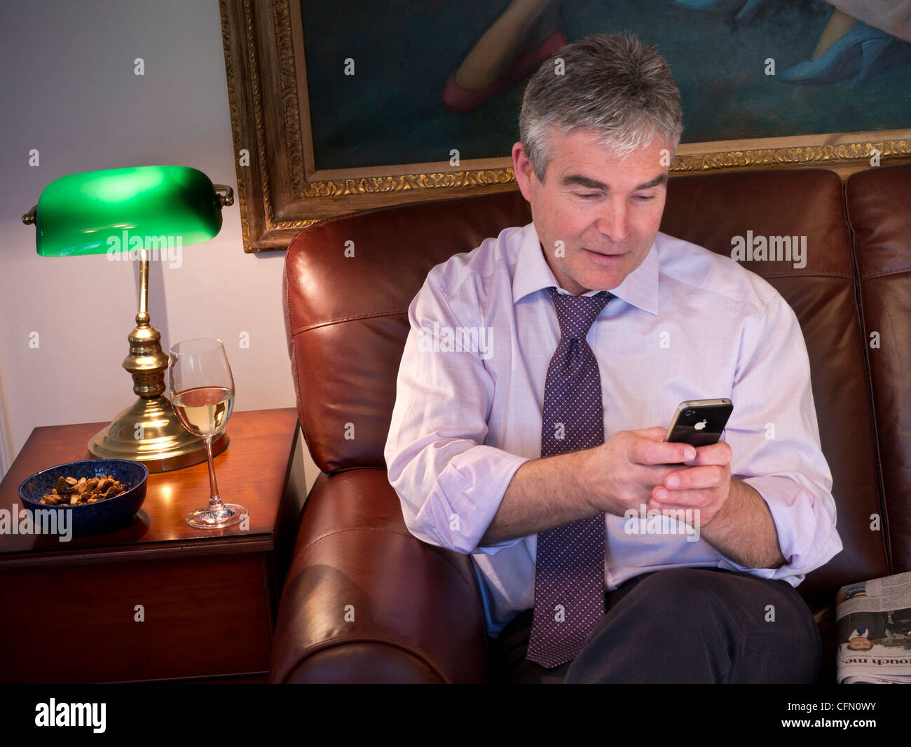 L'uomo rilassante sul divano di pelle in un tranquillo ambiente di lusso, utilizzando Apple iPhone smartphone Foto Stock
