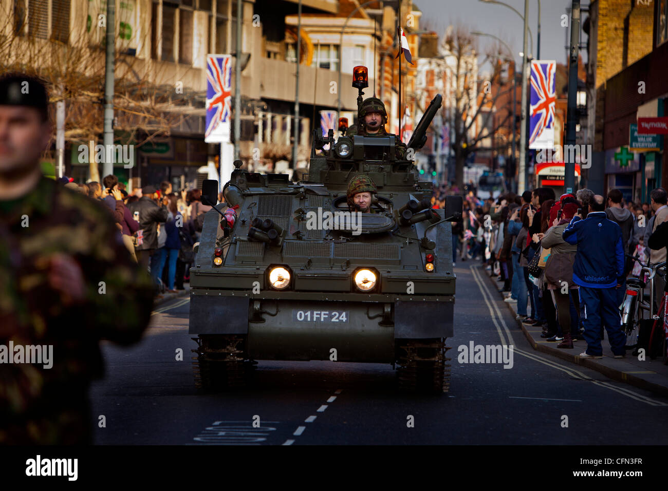 Truppe in veicoli blindati guidare passato High street negozi durante un Yeomanry Royal Parade, spettatori guarda dal marciapiede Foto Stock