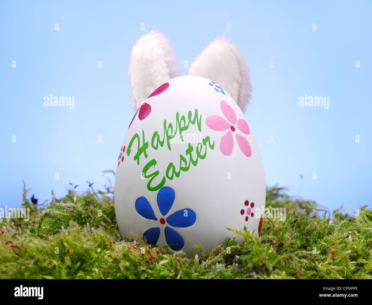 Uovo di Pasqua in erba con bunny orecchie degli inserimenti fuori da dietro oltre il cielo blu Foto Stock