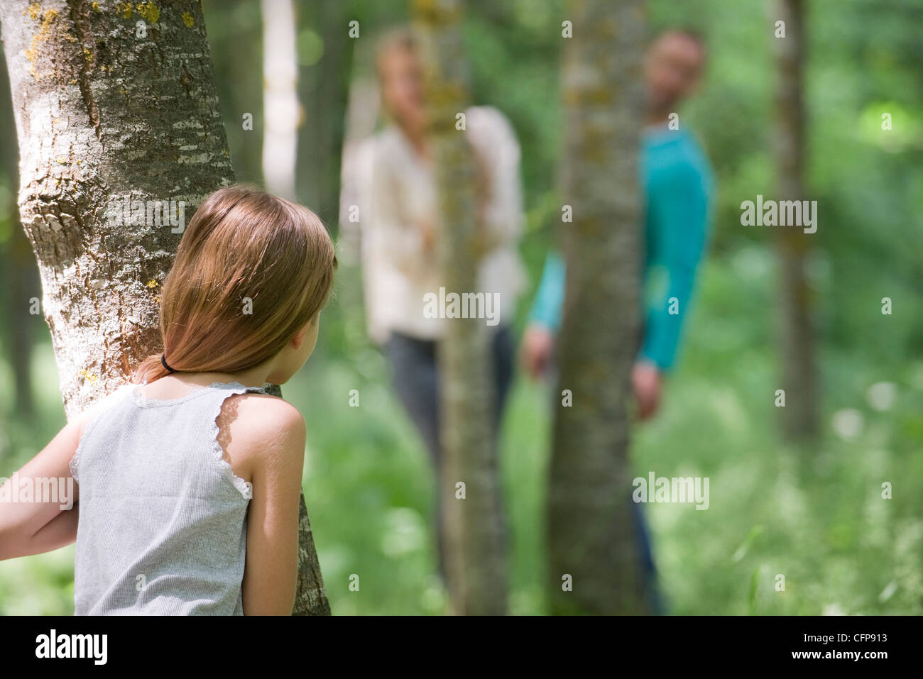 Ragazza di giocare a nascondino con i genitori nei boschi, vista posteriore Foto Stock