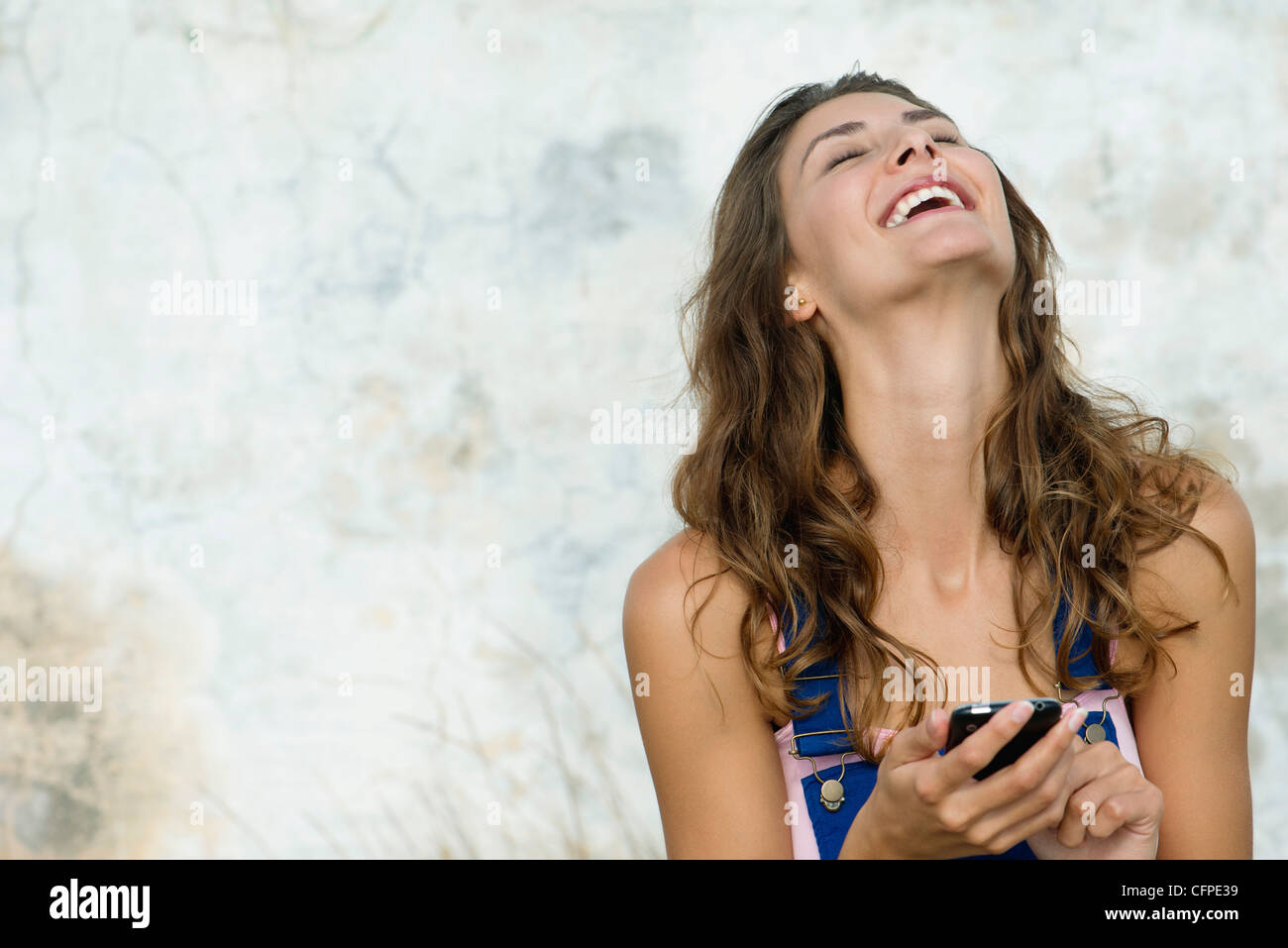 Giovane donna azienda telefono cellulare, ridendo Foto Stock