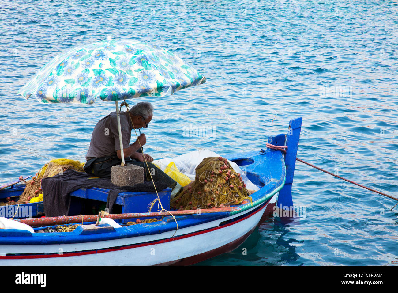 Tipico vecchio pescatore greco partecipando alle sue reti da pesca mentre ancora sulla sua barca per i prossimi giorni viaggio a Cefalonia Foto Stock