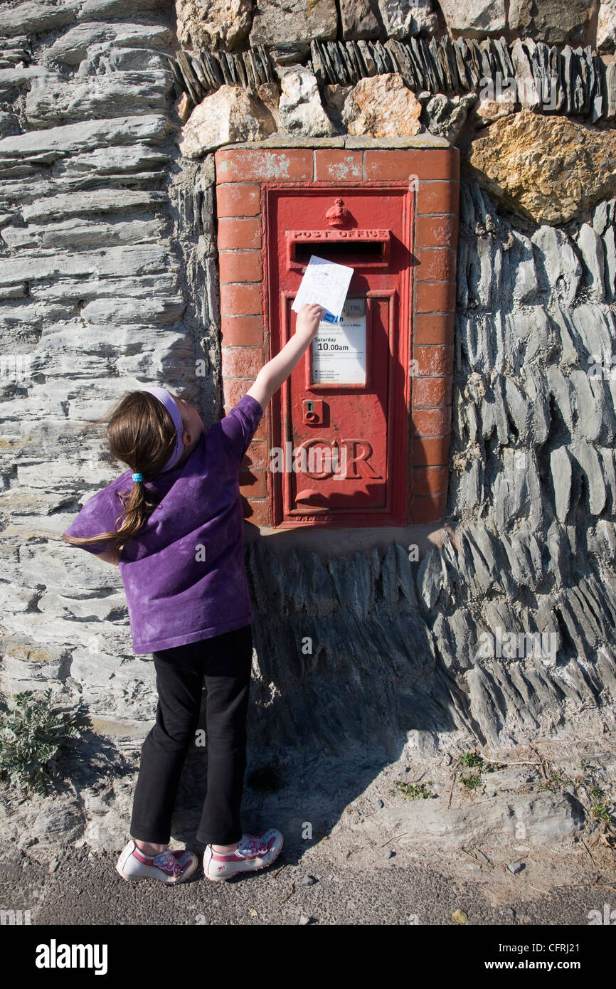 Bambina inviare cartoline in un rosso postbox in Woolacombe, Devon Foto Stock