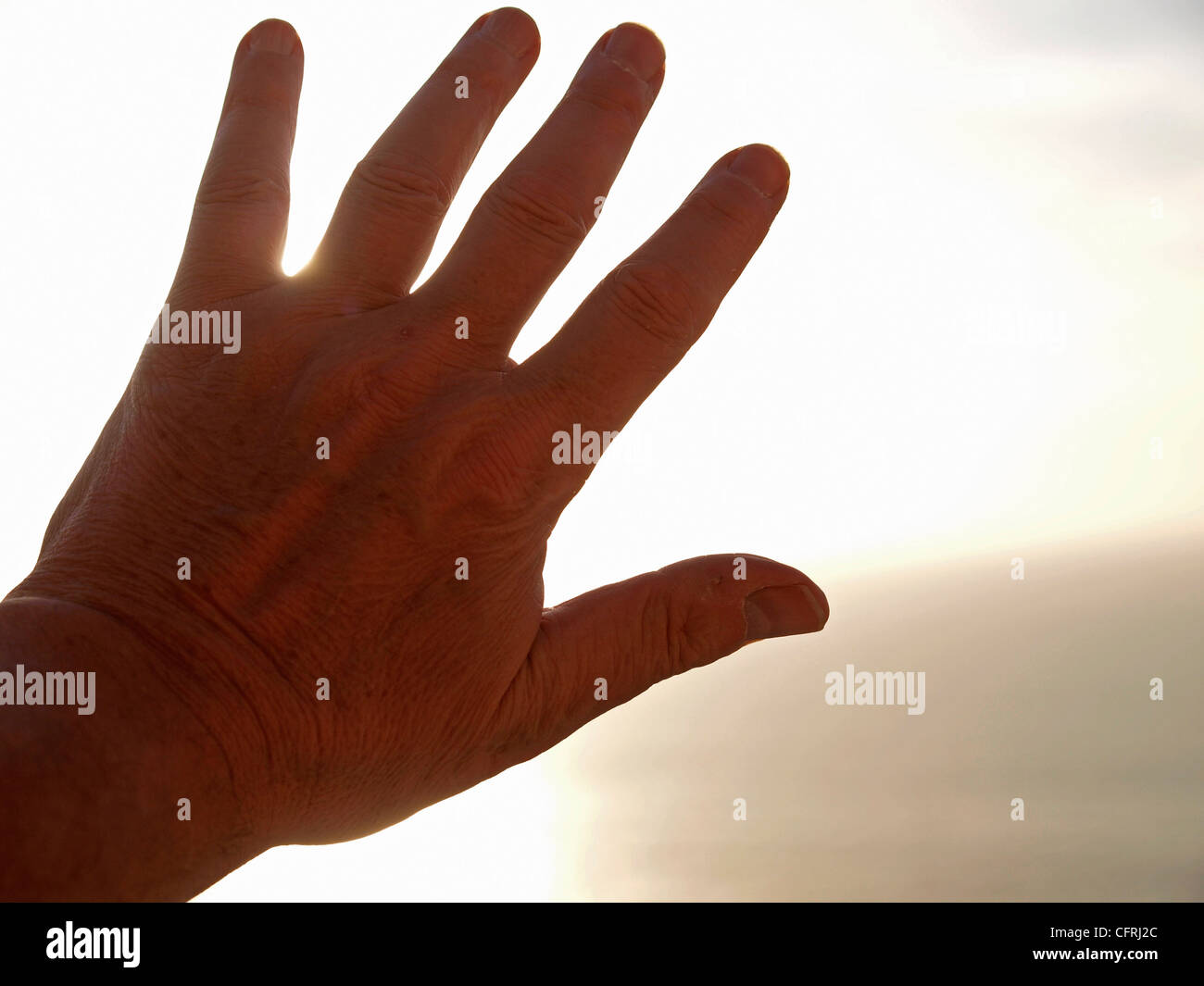 LA MANO SINISTRA DEL FOTOGRAFO SI ALZÒ VERSO L'IMPOSTAZIONE DEL SOLE OCCHI SHEILDING DALLA LUCE BRILLANTE, LOS GIGANTES, TENERIFE Foto Stock