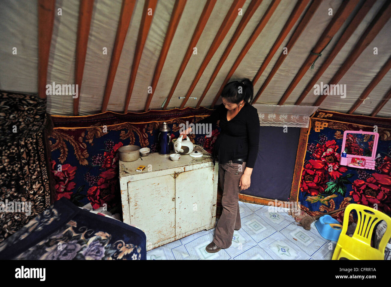 Mongolia, quartiere Baganuur entroterra, vista laterale di metà donna adulta in abbigliamento casual in piedi dal cabinet, tenendo il thermos in yurta Foto Stock