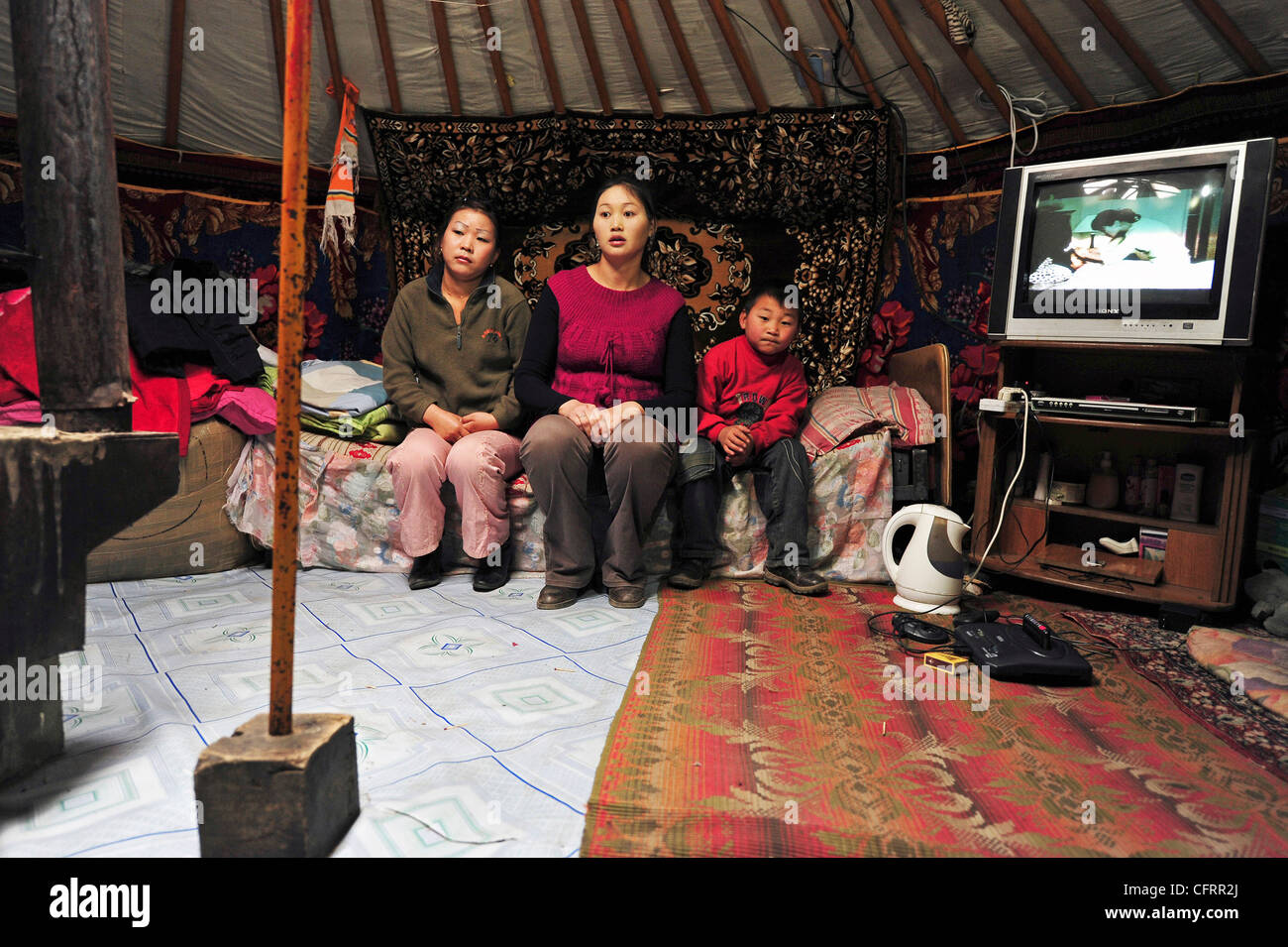 Mongolia, Baganuur, famiglia in abbigliamento casual, seduto sul divano in yurta dalla televisione e guardando lontano Foto Stock