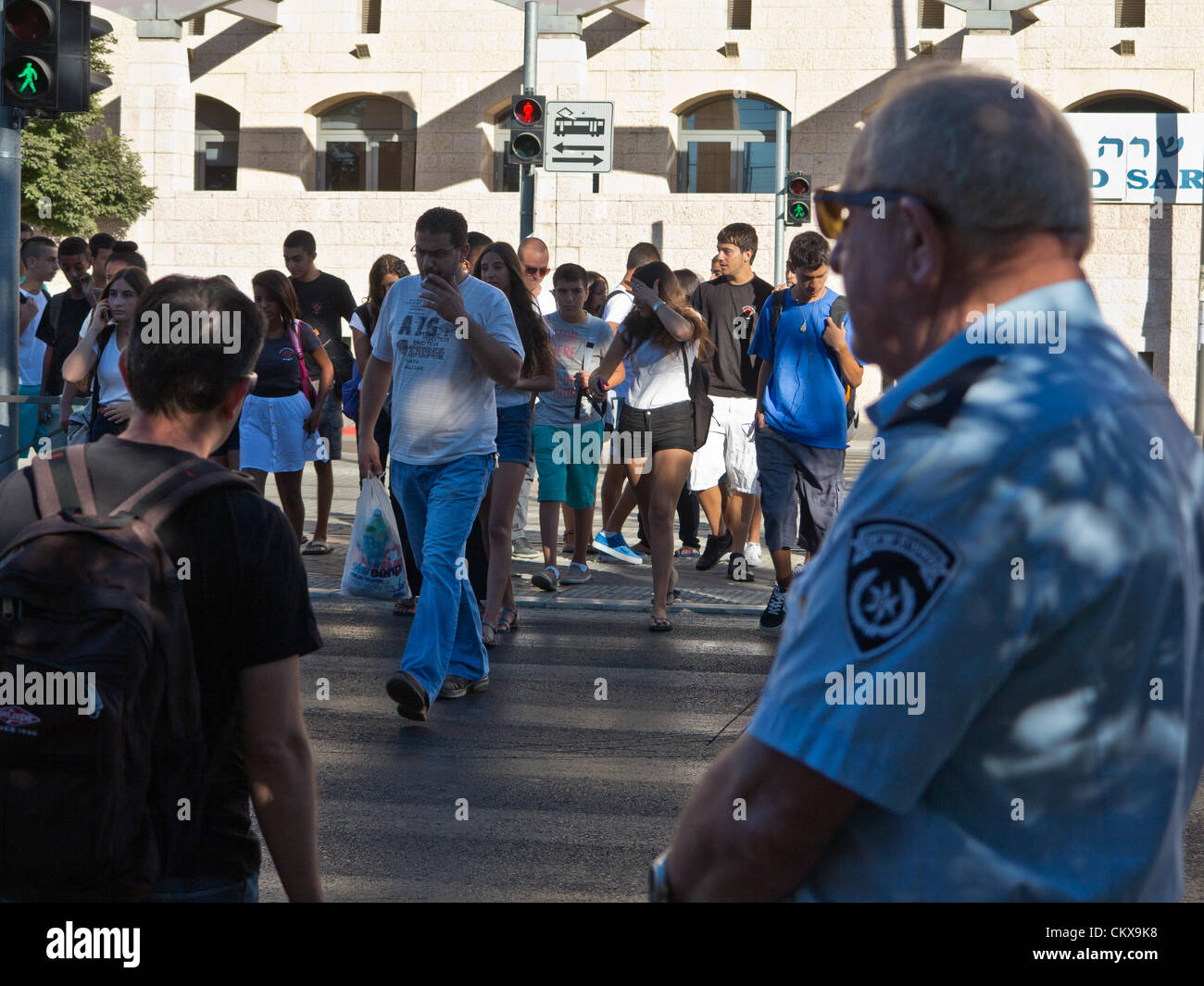 Il 27 agosto 2012. Un funzionario di polizia supervisiona un importante passaggio pedonale su Herzl Boulevard consentendo un accesso sicuro agli studenti nei pressi di Ziv alta scuola il primo giorno dell anno scolastico. Gerusalemme, Israele. 27-Aug-2012. Bambini israeliani di tornare a scuola oggi, abolendo il tradizionale sett. 1a data, in una prima fase delle riforme avviate dal Ministero dell'istruzione mira ad accorciare le vacanze estive a 6 settimane, parzialmente alleviare i genitori di enormi spese finanziarie. Foto Stock