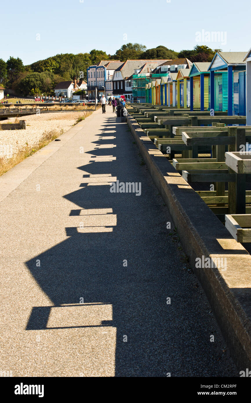 Whitstable, Inghilterra - 22 Settembre 2012: la tarda estate afternnoon sole proietta lunghe ombre della spiaggia di capanne lungo la costa di Whitstable, mentre il turista a godere di una passeggiata lungo la promenade. Foto Stock