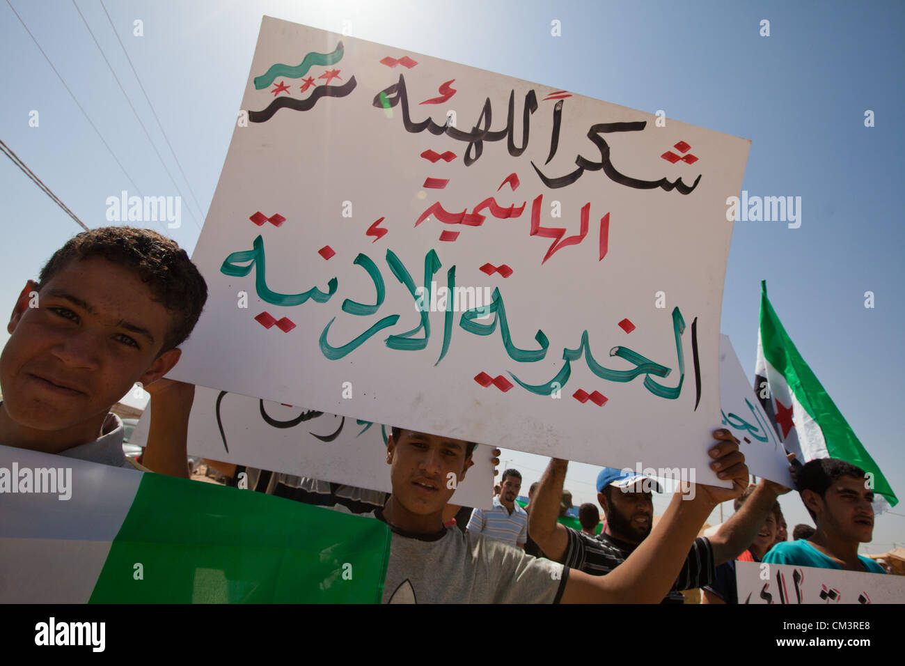 Anti Assad manifestanti marzo nelle strade al Zaatari Refugee Camp in Giordania giovedì 27 settembre 2012. Il vecchio stile bandiere siriane sono utilizzati. Segni di leggere "Grazie JHCO: Giordania Hashemita carità organizzazione' Foto Stock