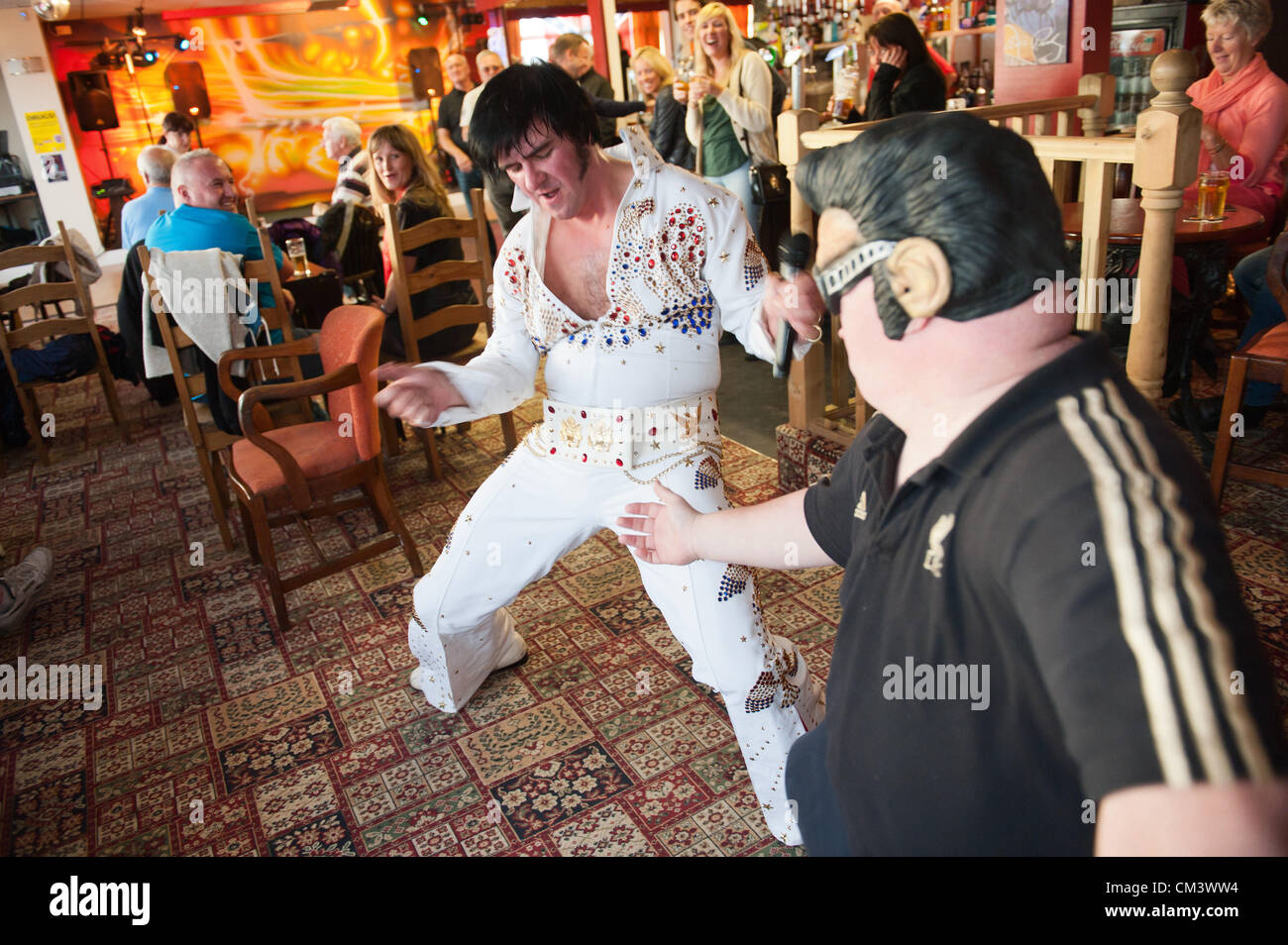 Il 28 settembre 2012. Porthcawl, Regno Unito. Robert Nash 33 Omaggio artista da Cardiff (L), esegue presso la cabina Pub ed è unita mediante una ventola Darren 'Elvis Tommaso 41 da Rhondda, Galles. Migliaia di fan di Elvis vestito di glitter tute, occhiali da sole oversize black ciuffi e basette scendono sulla piccola Victorian Galles del Sud località balneare per l'inizio del più grande festival di Elvis nel mondo. Nel corso di tre giorni, 100 mostra in diverse posizioni trasformerà questa tranquilla cittadina in un soggiorno omaggio al Re del Rock n' Roll. Photo credit: Graham M. Lawrence/Alamy Live News. Foto Stock