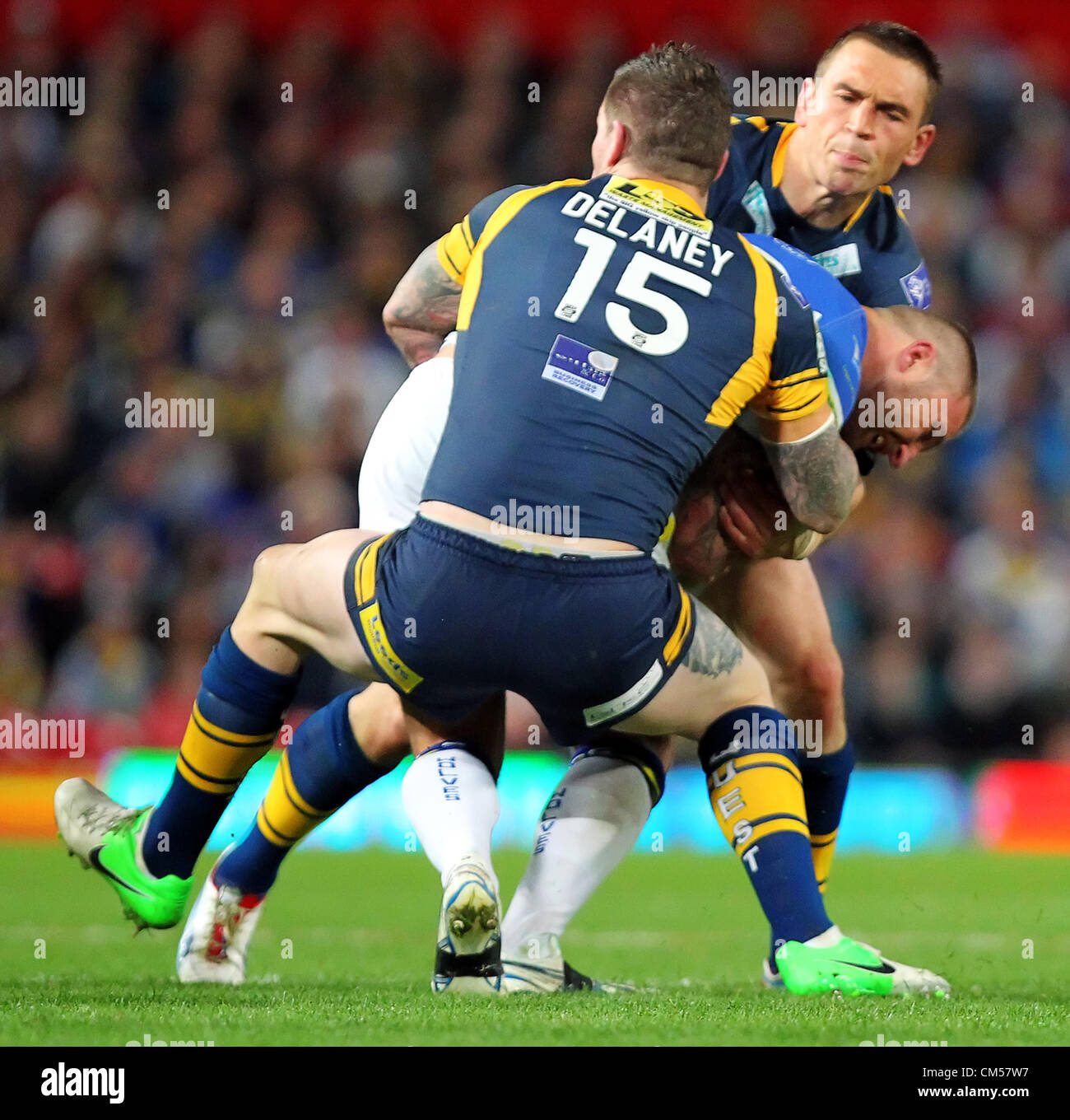 06.10.2012 Manchester, Inghilterra. Warrington lupi v Leeds rinoceronti. Warrington lupi inglese Prop Paolo poteri di legno attraverso un affrontare come Leeds rinoceronti allentato IN AVANTI Kevin Sinfield e Leeds rinoceronti seconda fila Brett Delaney provare a detenere lui durante la Stobart Super League Grand Final giocato a Old Trafford, Manchester. Foto Stock