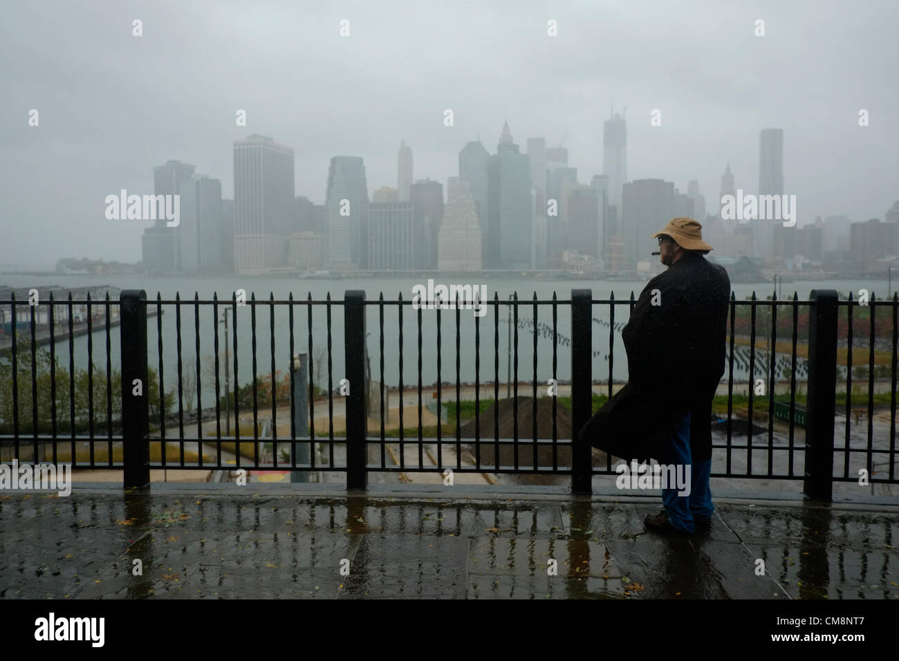 Ottobre 29, 2012, Brooklyn, NY, Stati Uniti. L'uomo fuma sigaro sulla Passeggiata di Brooklyn Heights come egli osserva uragano Sandy effetti sull'East River e Manhattan Foto Stock