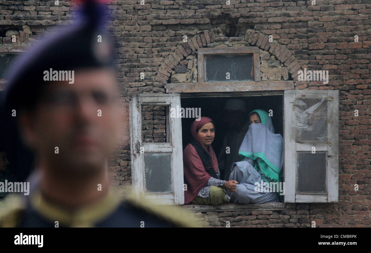 Luglio 13, 2012 - un musulmano del Kashmir donne siedono sulla finestra di una casa come poliziotti indiani in abito cerimoniale eseguire durante un evento al cimitero dei martiri a marchio "martiri giorno'' a Srinagar, l'estate capiatal del Kashmir indiano su 13,7, 2012. Negozi e attività sono rimaste chiuse in Srinagar il venerdì come separatisti del Kashmir chiamato per uno sciopero in occasione della ricorrenza del 13 luglio 1931 uccisione di decine di Kashmiris ucciso dalla polizia durante una manifestazione di protesta contro il Hindu Maharaja Hari Singh, allora dominatore della regione himalayana. Il Kashmir Stato governo osserva inoltre la giornata come martire Foto Stock