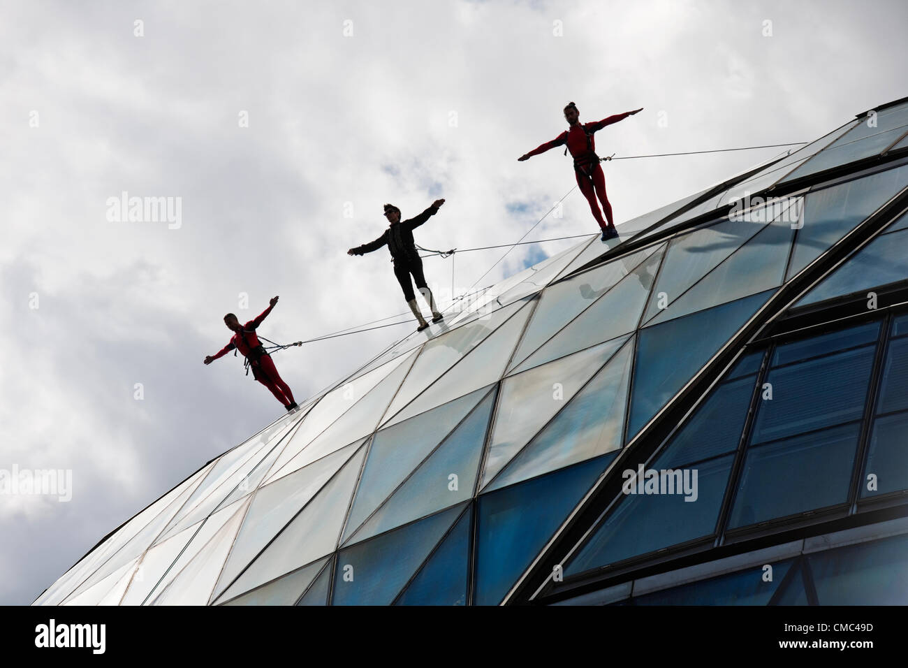 Domenica 15 Luglio, Municipio di Londra. Il leggendario New York coreografo, Elizabeth Streb e la sua compagnia di ballo eseguire un giro sulle alture della City Hall di Londra di questa mattina in vista degli anelli olimpici appesi da Tower Bridge. I giochi olimpici inizia a Londra il 27 luglio e questo evento fa parte delle olimpiadi culturali. Foto Stock