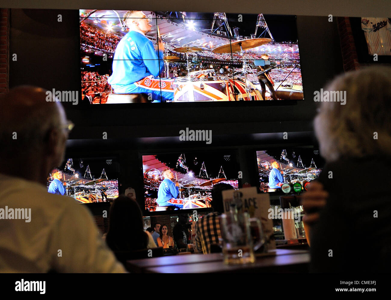 Alcune persone guarda la band Arctic Monkeys prestazioni durante i Giochi olimpici di Londra 2012 Cerimonia di apertura, prevista per essere visualizzati in diretta TV a livello mondiale da un pubblico di oltre un miliardo di persone, fotografato in una gabbia aux sports bar sulla luglio 27, 2012 a Montreal, Canada. Foto Stock