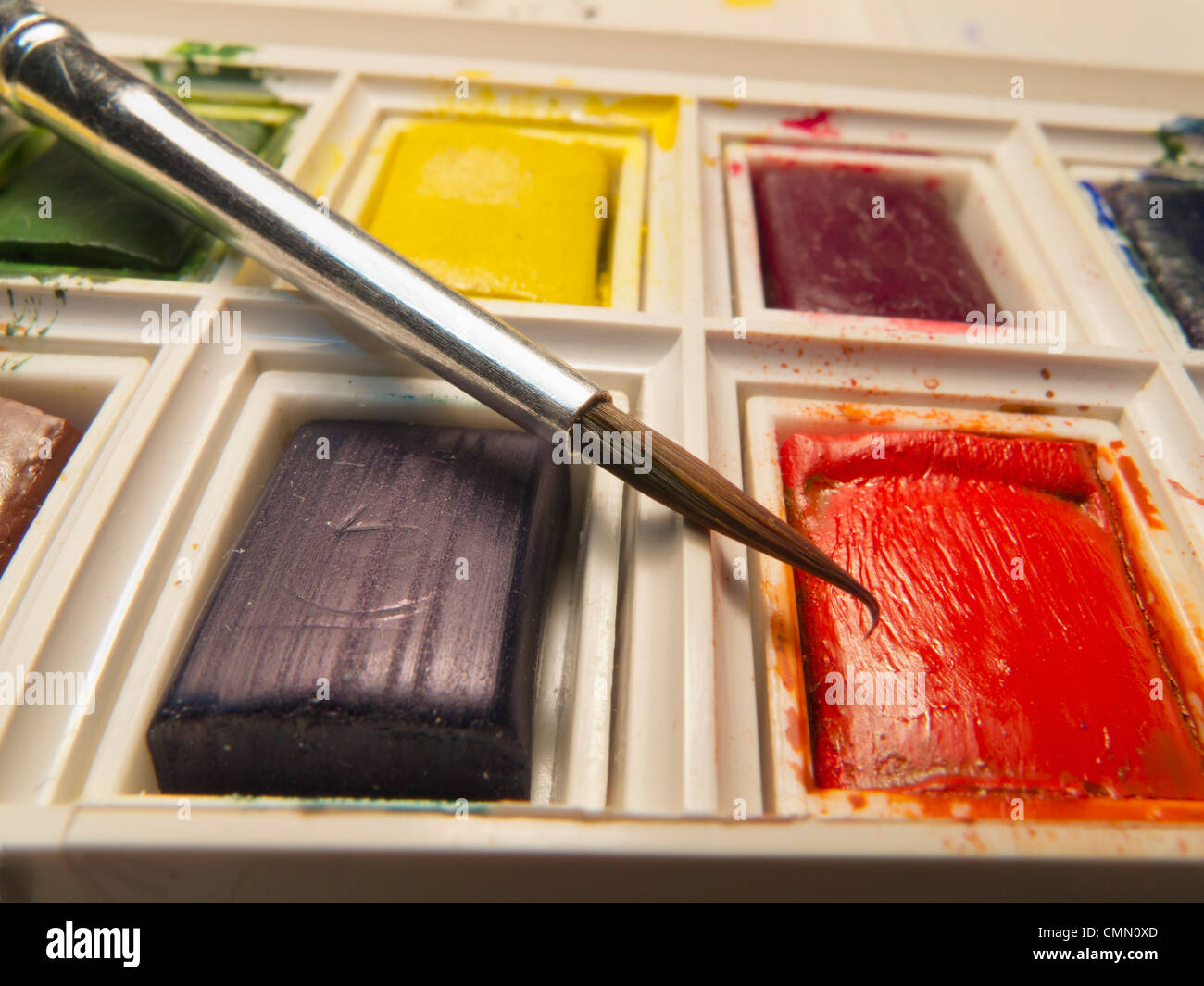 Primo piano della spazzola in bilico sopra compressa di rosso il colore dell'acqua in una scatola di vernice. Foto Stock
