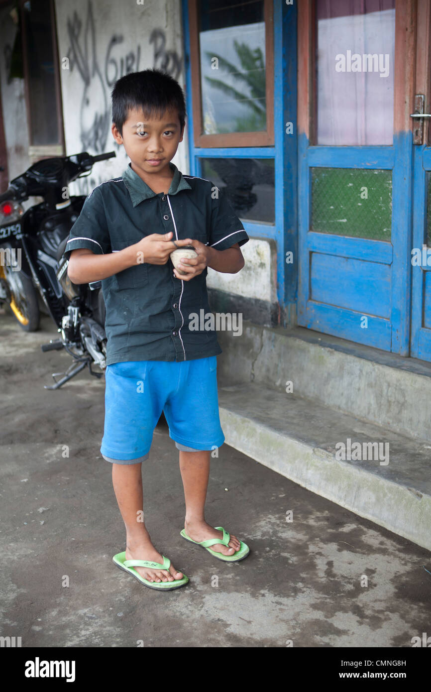 Un ragazzo Balinese riproduce la parte anteriore della sua casa con un legno top di filatura. Foto Stock