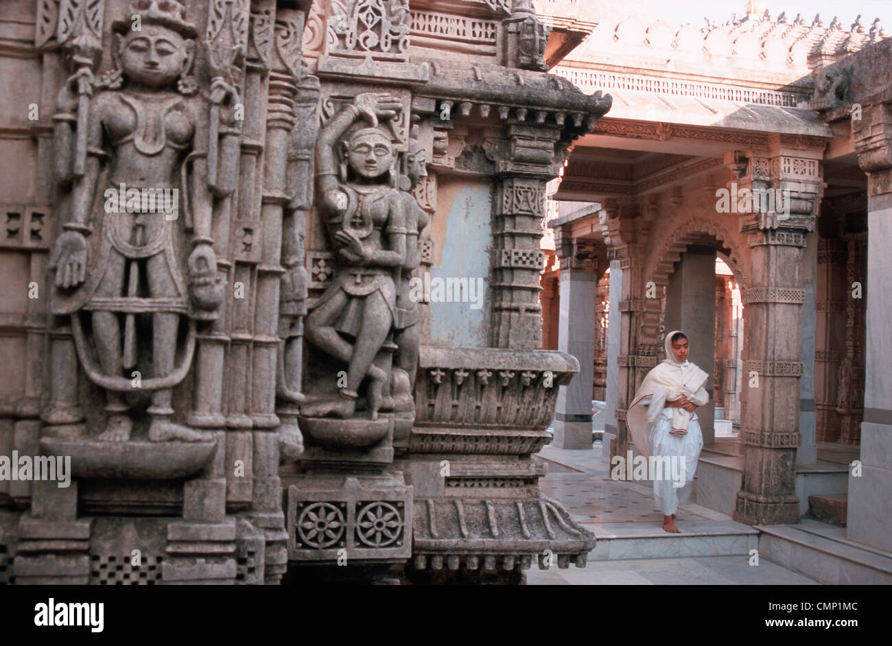 Jaïn nun camminando in un tempio con sculture in primo piano ( India) Foto Stock