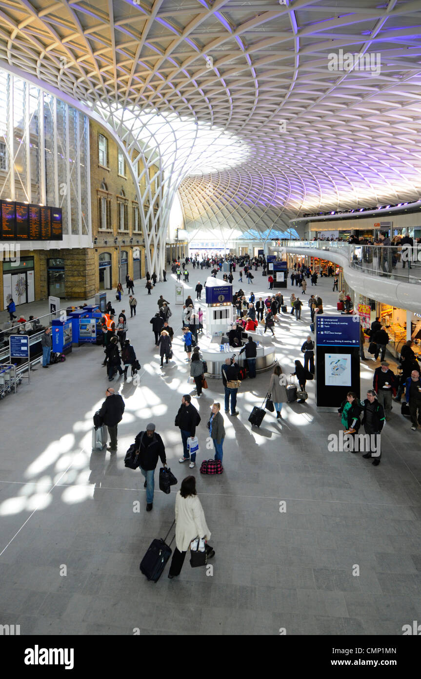 I passeggeri del treno si trovano nell'atrio di partenza della stazione ferroviaria di Kings Cross, con piano rialzato e struttura interna a motivi geometrici del tetto illuminata Londra Regno Unito Foto Stock