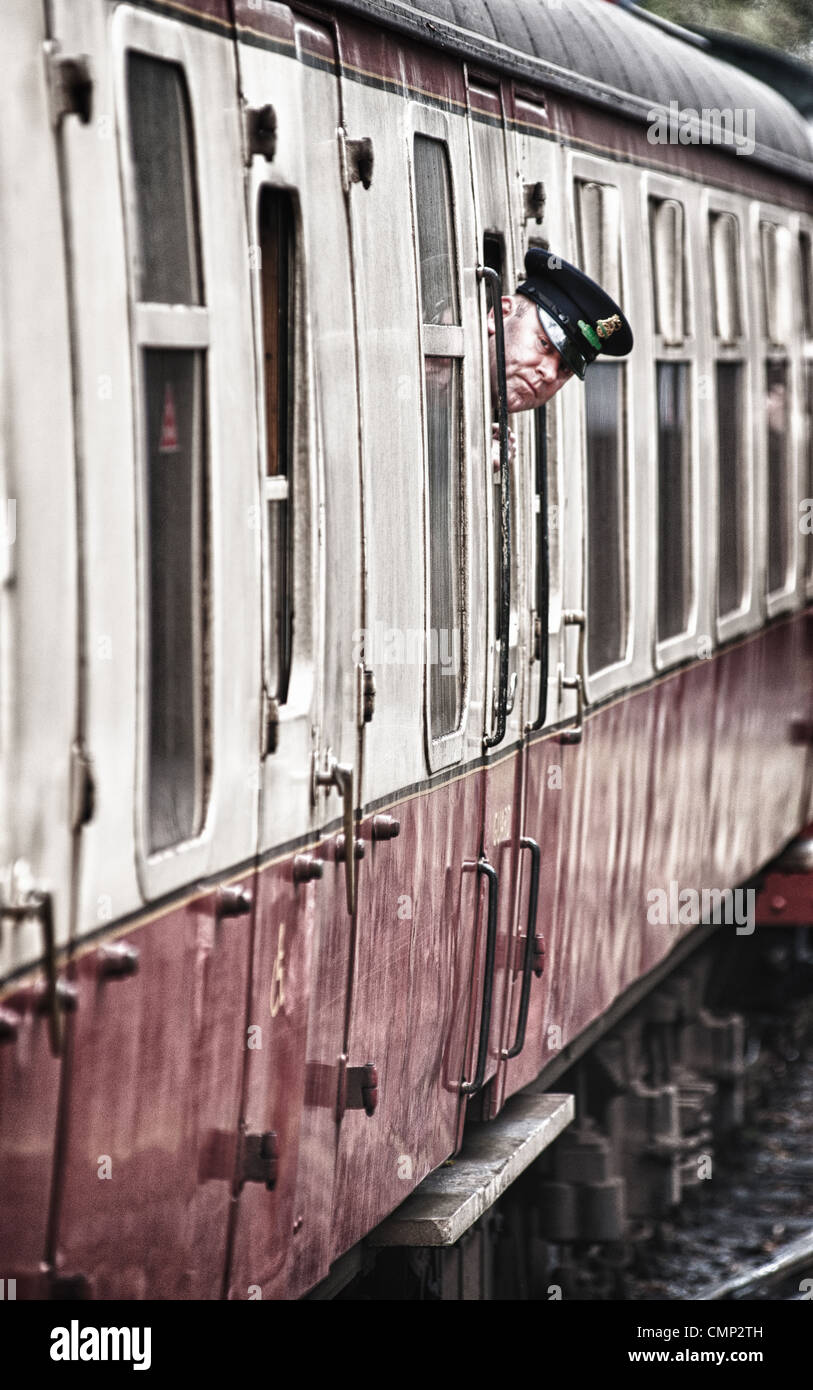 Una guardia gli blocca la testa fuori dal finestrino come un treno si avvicina Wenford station Foto Stock