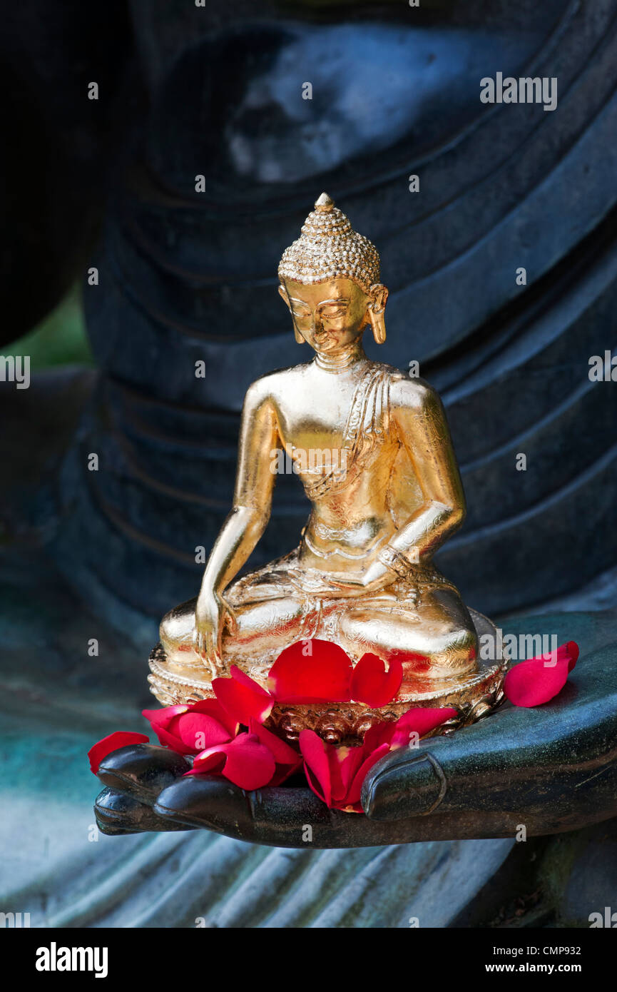 Golden statua del Buddha e il rosso dei petali di rosa sul lato di una grande statua del Buddha Foto Stock