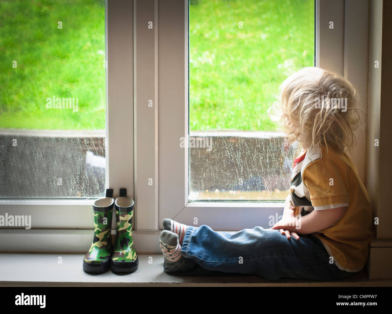 Ragazzo a guardare la pioggia attraverso una finestra Foto Stock