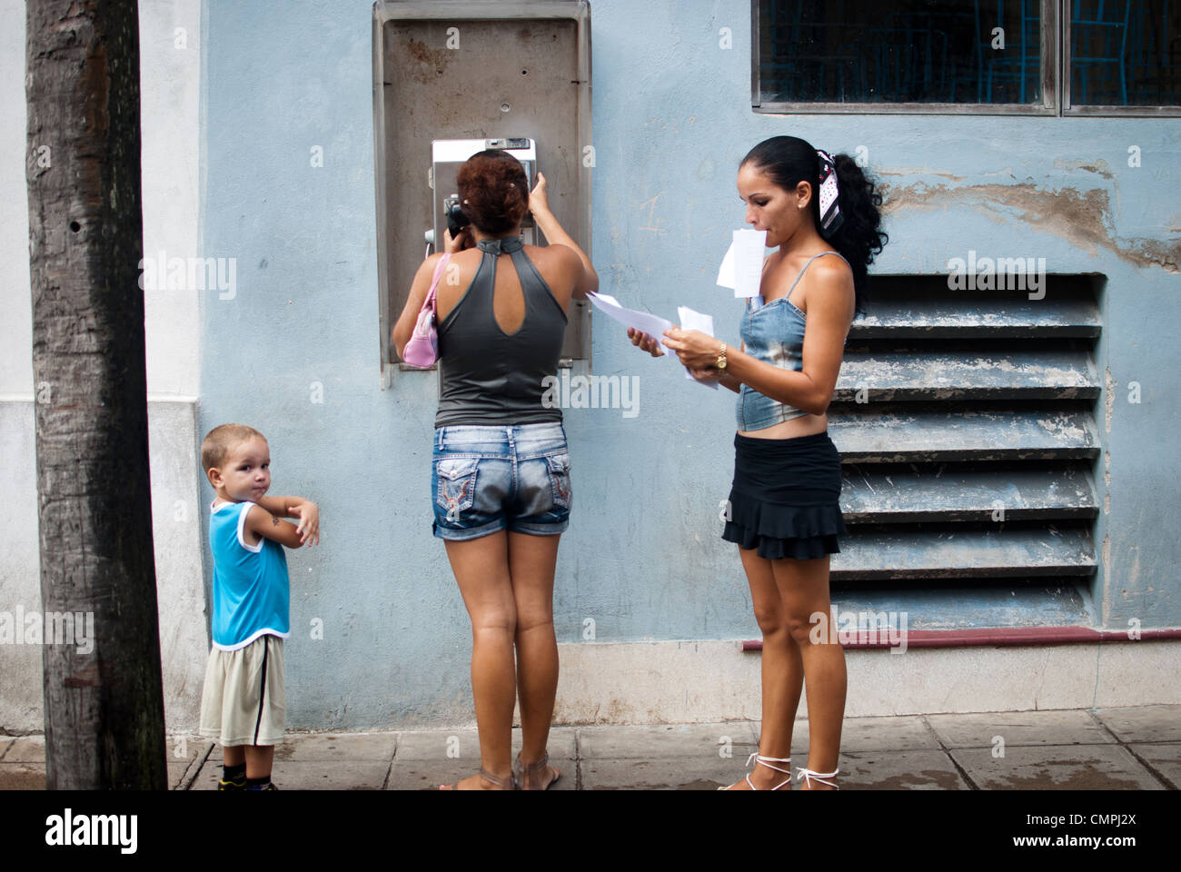 Le persone che usano un telefono pubblico, signora azienda carte importanti nel suo mese e le mani cercando di ordinarli, Cuba Foto Stock