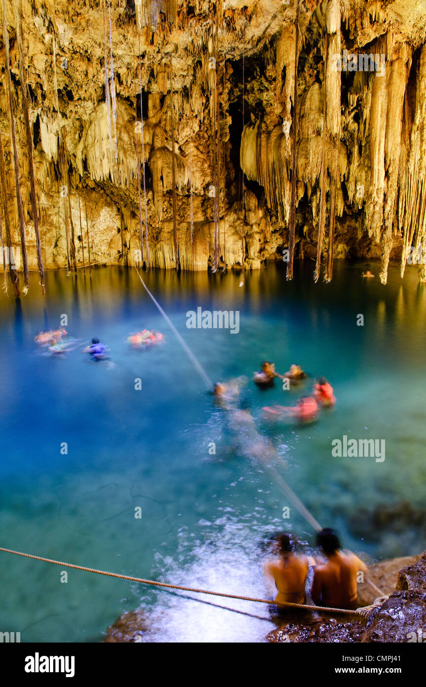 VALLADOLID, Messico - Nuotatori godervi le acque cristalline del Cenote X'kakah vicino a Valladolid (anche nei pressi di Dzitnup). Parte dello Yucatan e la grande rete di vie navigabili della metropolitana che passano attraverso il calcare poroso, Cenote X'kakah è un popolare piscina sotterranea foro. Esso ha una piccola apertura nel soffitto che consente alla luce, aria fresca, e anche un po' di pioggia, e impressionanti stalattiti che pendevano dal soffitto. La temperatura dell'acqua è una costante a 76 gradi fahrenheit per tutto l'anno. Foto Stock