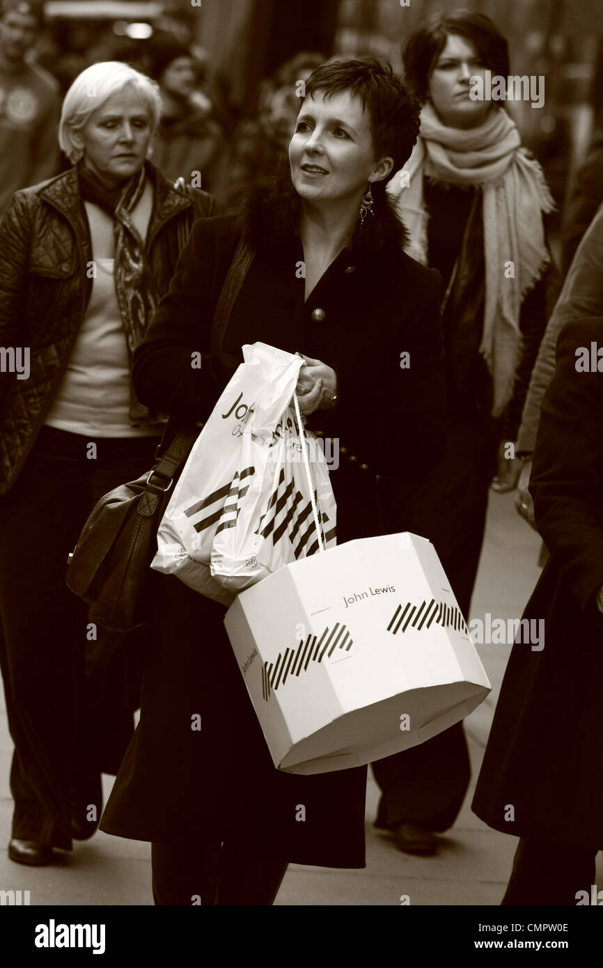 Una femmina di shopper portante un John Lewis shopping bag e box - gli altri acquirenti in background Foto Stock