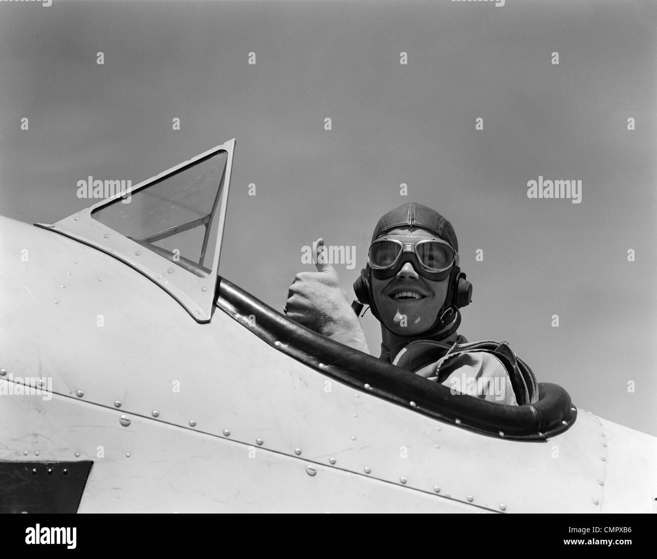 1940s sorridente esercito aria CORPS pilota nel pozzetto aperto indossando un cuoio battenti casco dando un pollice in alto segno Foto Stock