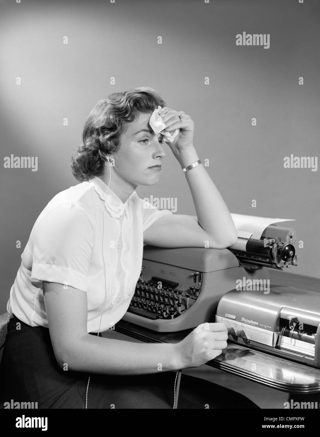 Anni Cinquanta donna sofferente Segretario seduto alla scrivania con i nastri inchiostratori per macchine da scrivere e macchine di dettatura HOLDING fazzoletto di fronte Foto Stock