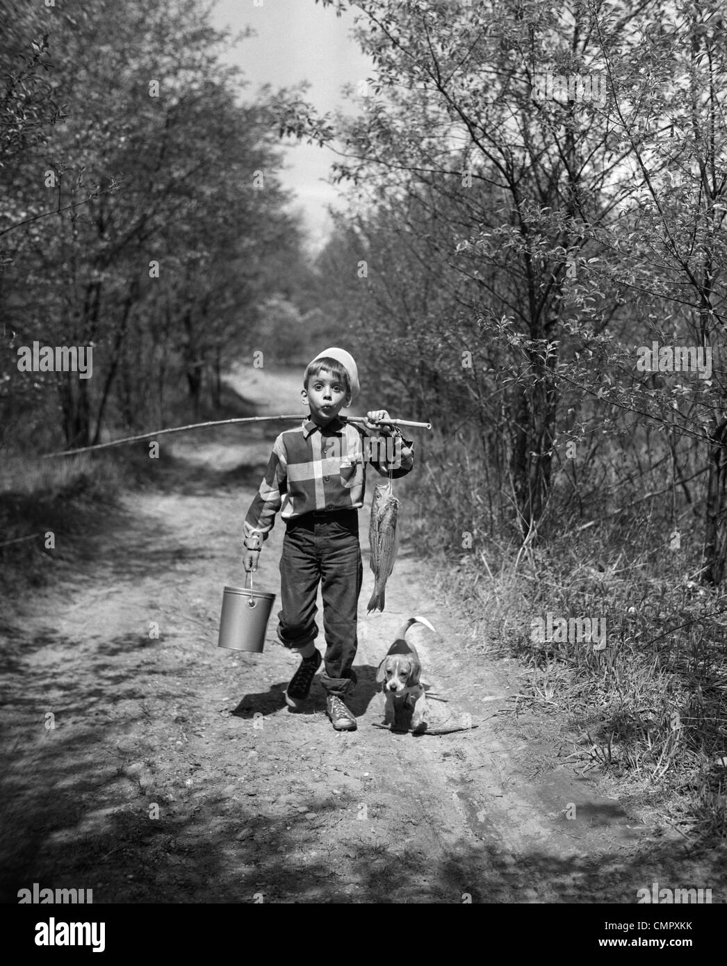 Anni Cinquanta BOY BEAGLE cucciolo di camminare per strada di campagna che porta il fischio pesca polo secchio di pesci Foto Stock