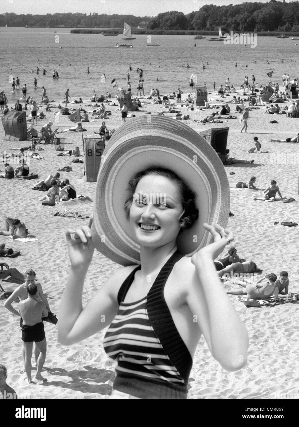 1930s VACANZA MONTAGE ritratto donna sorridente IN COSTUME DA BAGNO indossando grande cappello di paglia e la scena della spiaggia affollata Foto Stock