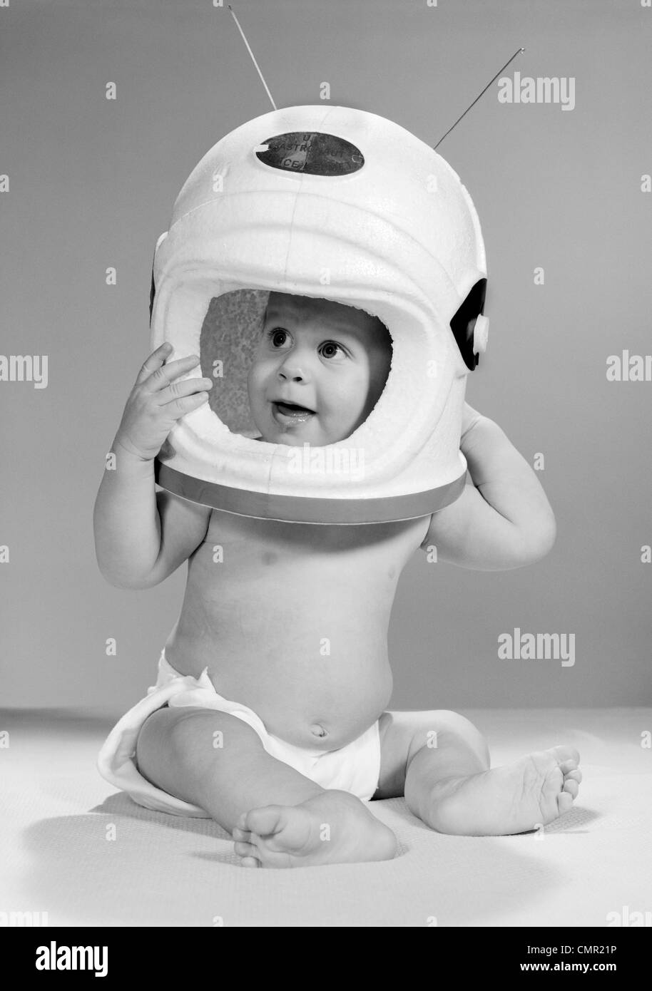 Anni sessanta BABY nel pannolino seduto tenendo astronauta casco con antenne sulla testa Foto Stock