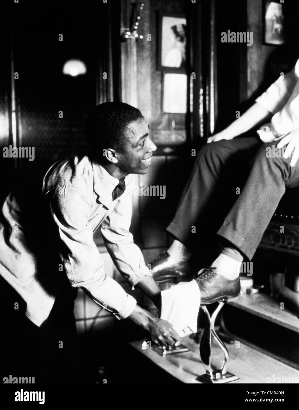 1930s African American uomo sorridente SHINING SCARPE sul Patrono seduto al cavalletto di lucidatura scarpe Foto Stock