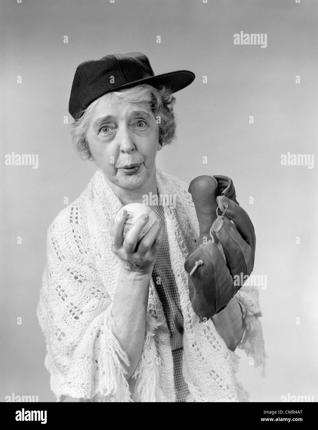 Anni Cinquanta anni sessanta la nonna con berretto da baseball & guanto attorno alla sfera del passo guardando la fotocamera Foto Stock