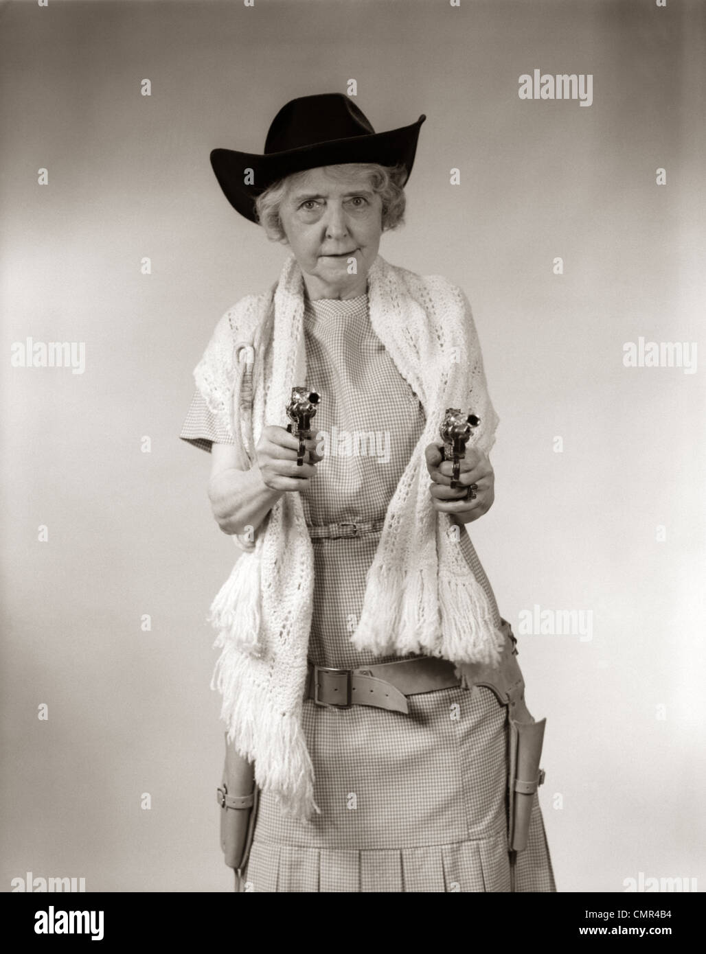 Anni Cinquanta GRANNY COWGIRL indossando cappello e scialle & puntando 2 pistole e guardando la fotocamera Foto Stock