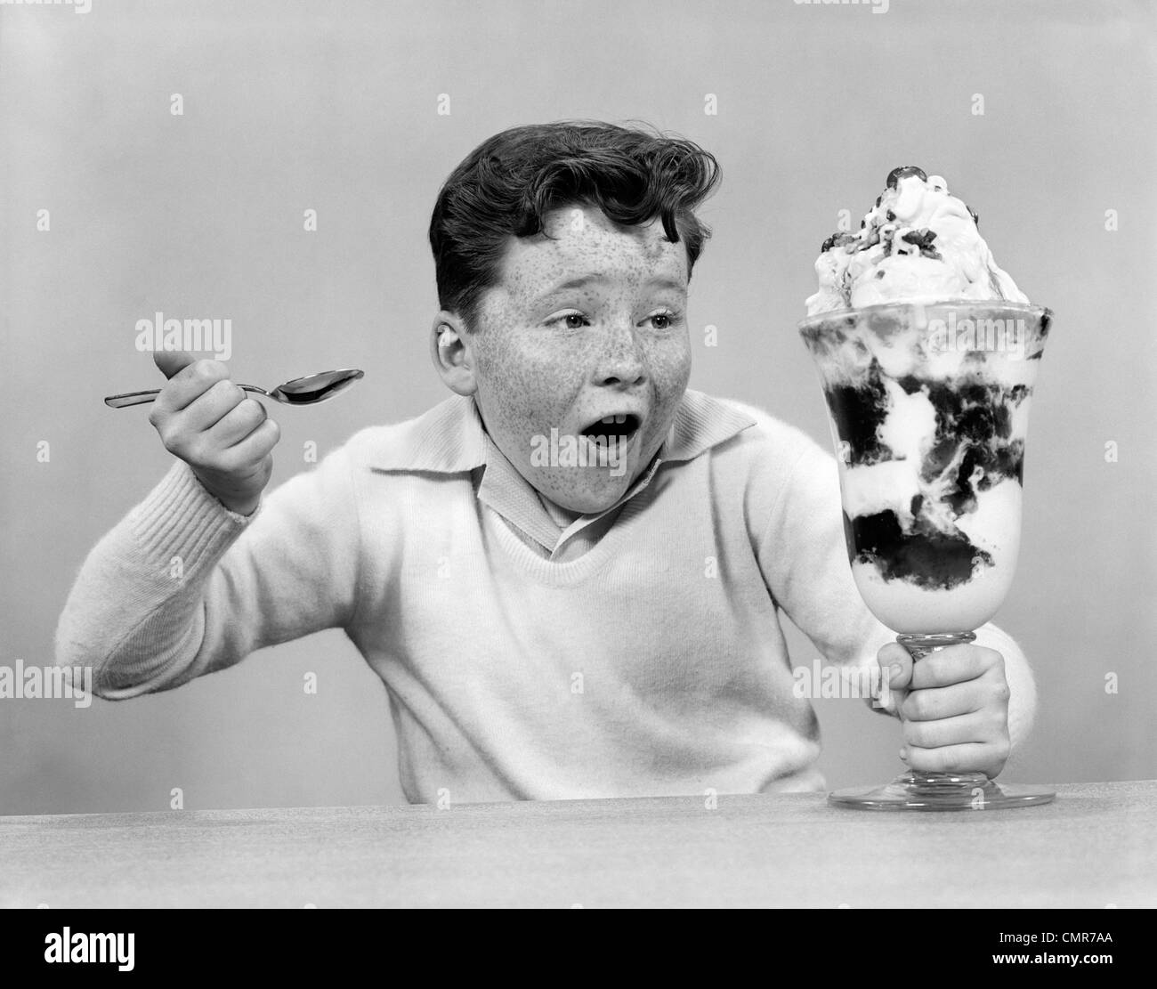 Anni Cinquanta FRECKLE FACE BOY scavando nel ghiaccio gigante di gelato di crema Foto Stock