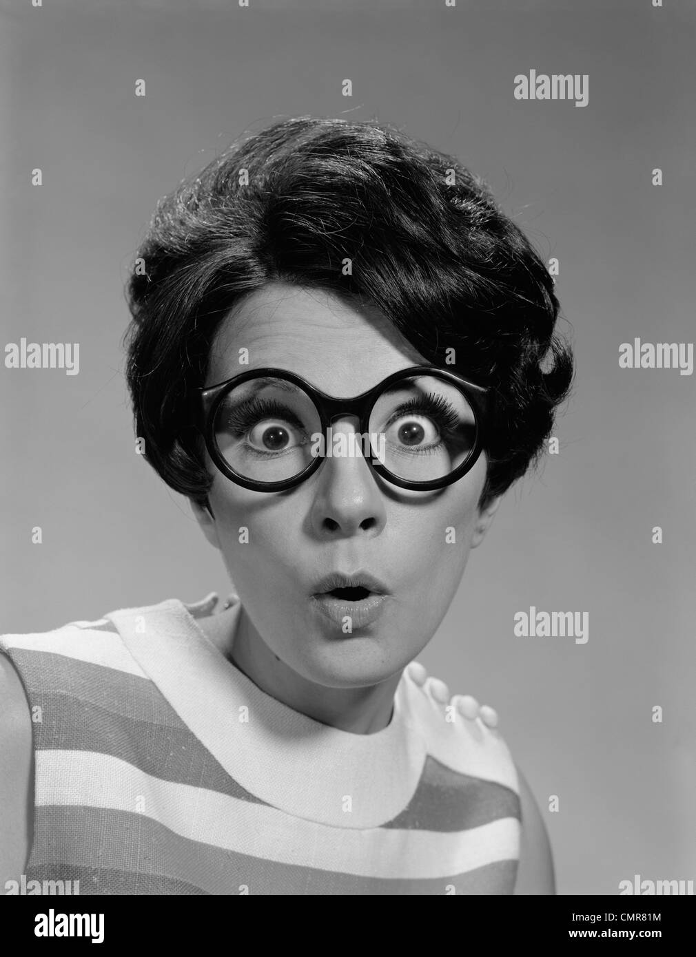 Anni sessanta ritratto BRUNETTE indossando spessi scuro ROUND occhiali con occhi spalancati Foto Stock
