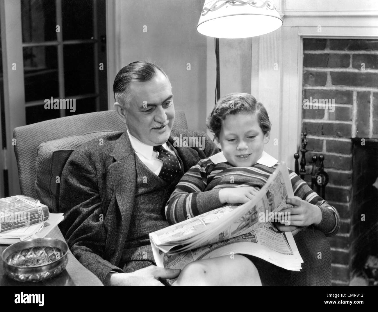 1930s 1940 nonno seduto con il nipote in giro la lettura di giornale della domenica COMICS INSIEME IN SALOTTO Foto Stock