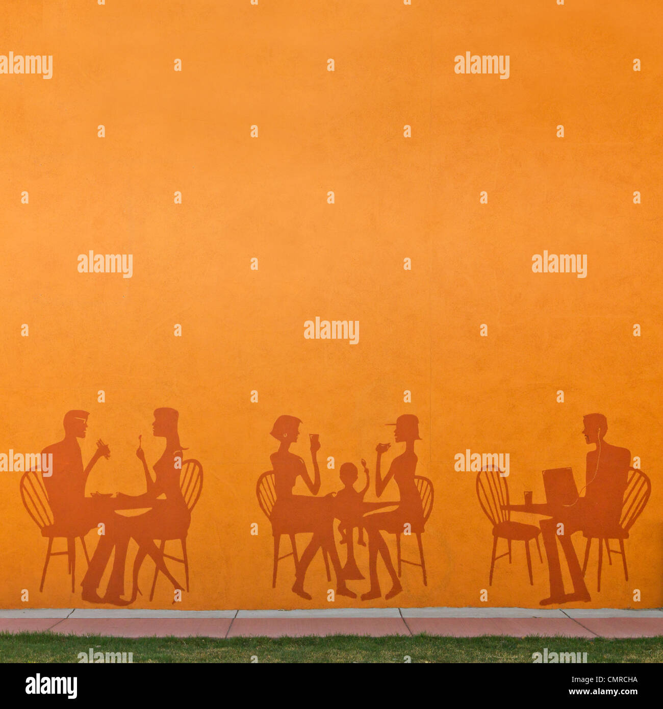Sagome di persone di mangiare in un ristorante dipinta su un muro arancione con una città marciapiede davanti. Foto Stock