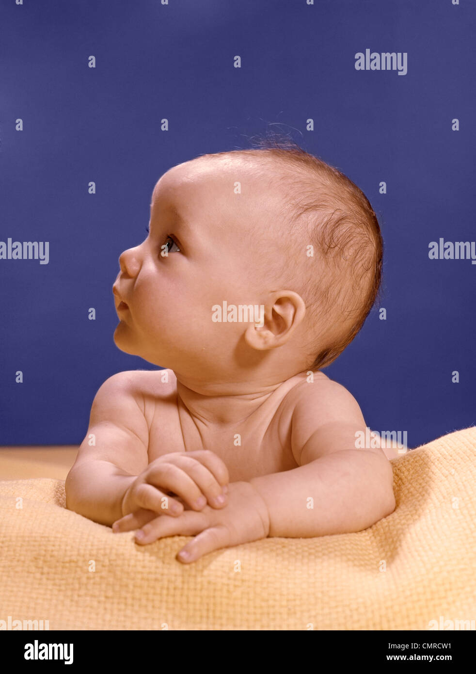 Anni sessanta Ritratto di bambino Sulla coperta di giallo appoggiato su bracci ripiegati testa voltata a destra guardando verso l'alto Foto Stock