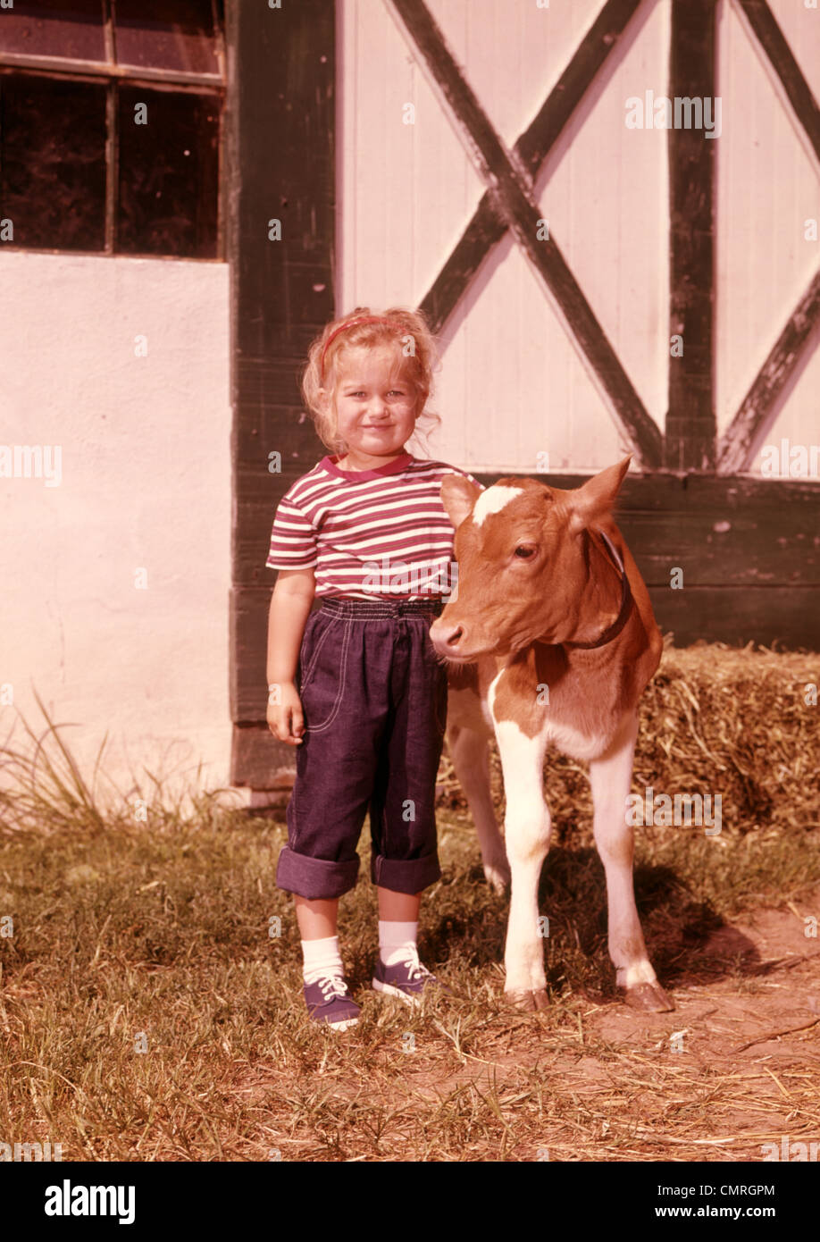 Negli anni sessanta la ragazza sorridente arrotolato jeans denim con l'isola di Guernsey vitello granaio esterno Foto Stock
